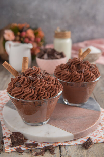 Mousse al cioccolato servita in coppa con ciuffi di crema, scaglie di cioccolato e un wafer