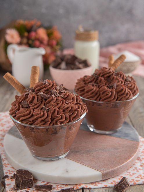 Mousse al cioccolato servita in coppa con ciuffi di crema, scaglie di cioccolato e un wafer
