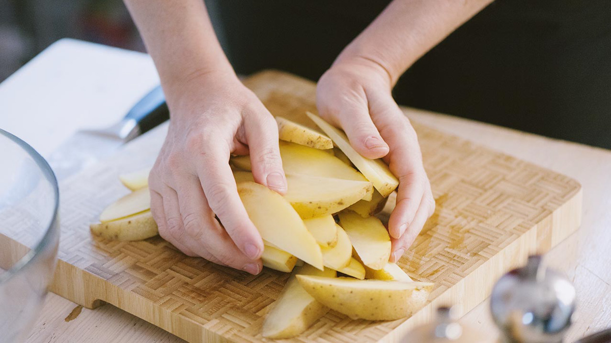 Mani che raccolgono spicchi di patata tagliati sul tagliere