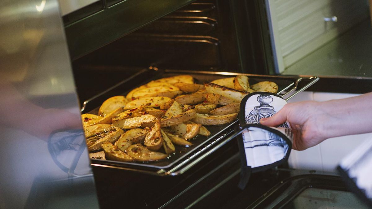 Teglia di patate al forno con erbe aromatiche estratta dal forno con presina