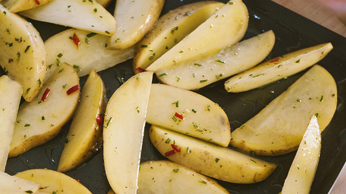 Spicchi di patate crude conditi con erbe tritate e peperoncino rosso, pronti per la cottura
