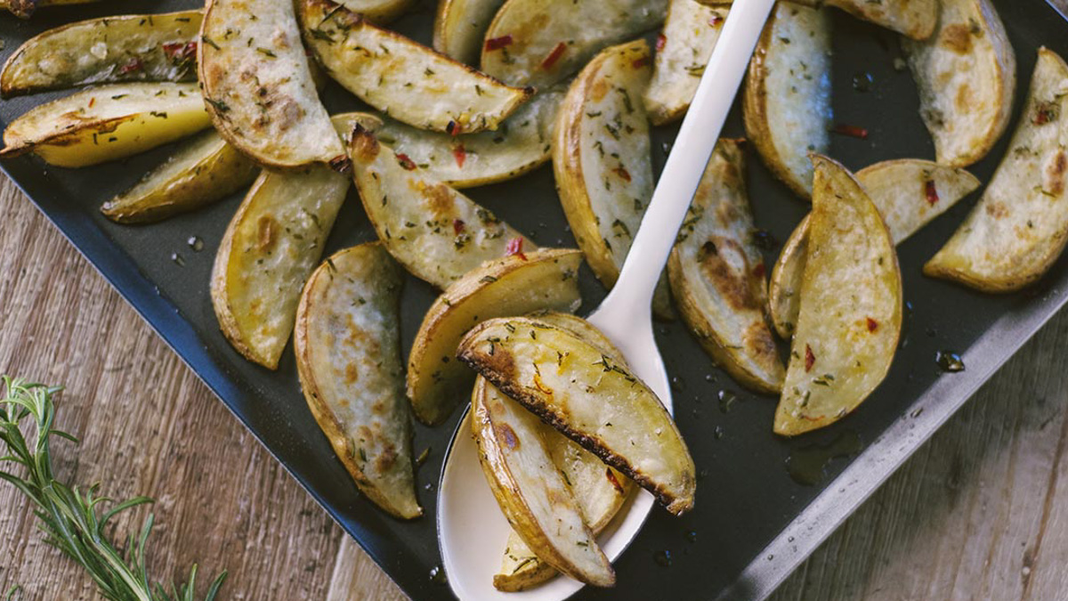 Spicchi di patate al forno dorati con rosmarino e peperoncino, serviti con un cucchiaio