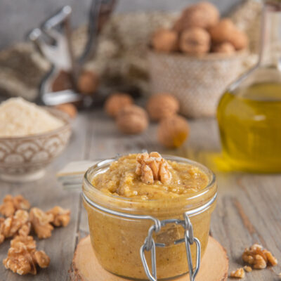 Pesto di noci in vasetto con gheriglio intero in superficie e noci sparse intorno