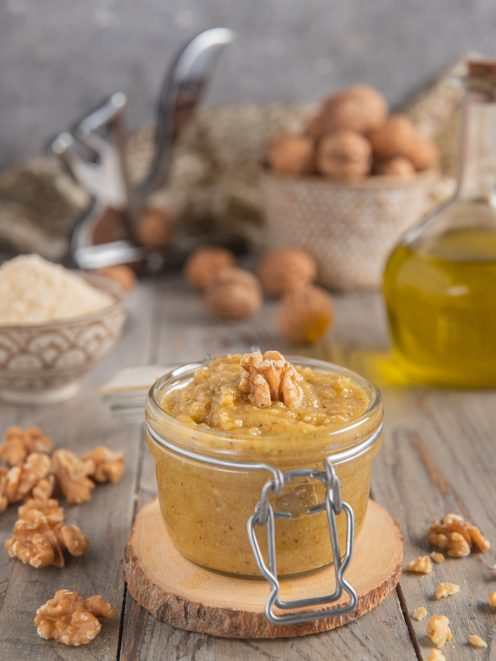 Pesto di noci in vasetto con gheriglio intero in superficie e noci sparse intorno
