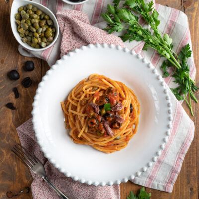 Spaghetti al sugo alla puttanesca con olive nere, capperi e acciughe, guarniti con prezzemolo fresco