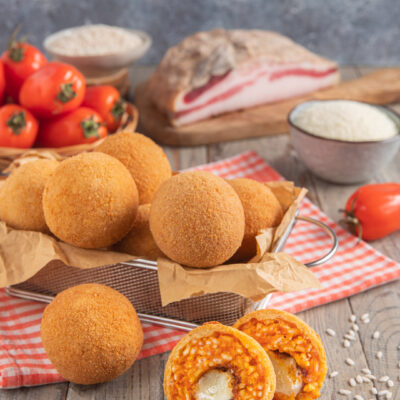 Arancini all'amatriciana dorati e croccanti, uno tagliato a metà mostra riso al sugo e mozzarella filante