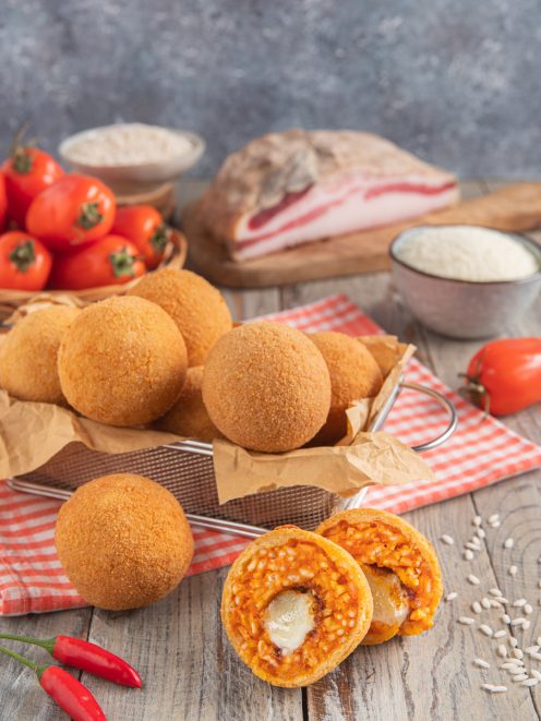 Arancini all'amatriciana dorati e croccanti, uno tagliato a metà mostra riso al sugo e mozzarella filante