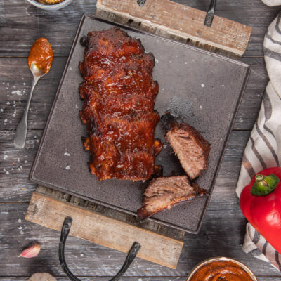 Costine di maiale in salsa barbecue glassate e affumicate, con due pezzi tagliati che mostrano la carne al suo interno