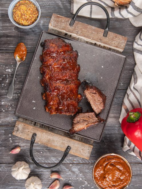 Costine di maiale in salsa barbecue glassate e affumicate, con due pezzi tagliati che mostrano la carne al suo interno