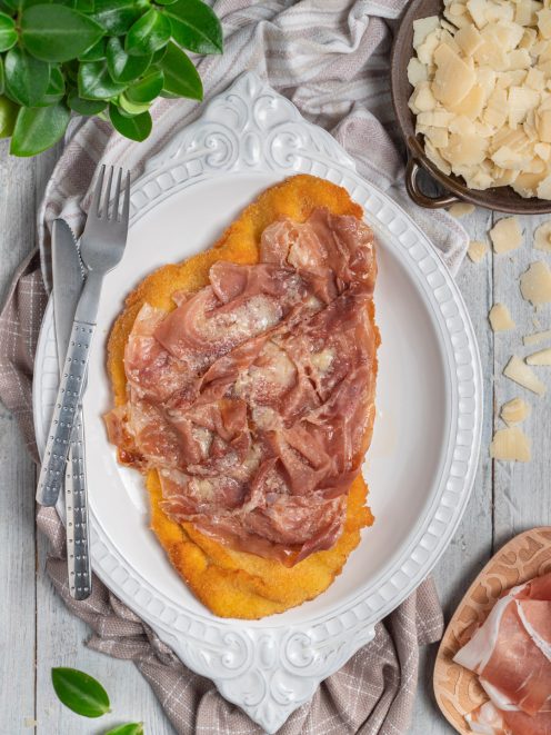 Cotoletta alla bolognese impanata e fritta, coperta di prosciutto crudo e scaglie di formaggio