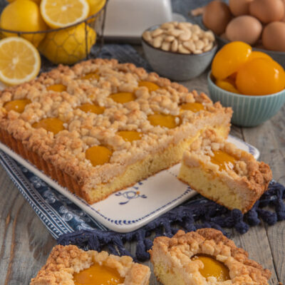 Crumble cake alle pesche con streusel dorato e fette tagliate che mostrano l'interno soffice