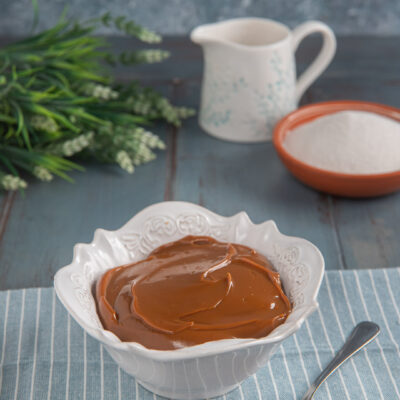 Dulce de leche cremoso e lucido servito in una ciotola, con un cucchiaio a lato