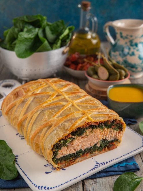 Filetto di salmone in crosta sfogliata tagliato a meta, con ripieno di spinaci e pomodorini secchi