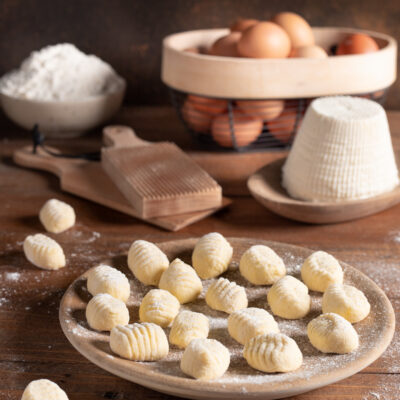 Gnocchi di ricotta crudi con rigatura, spolverati di farina accanto a uova e ricotta fresca