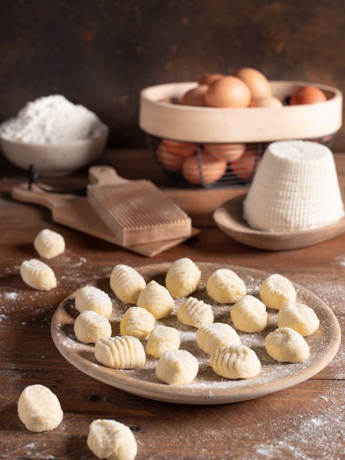 Gnocchi di ricotta crudi con rigatura, spolverati di farina accanto a uova e ricotta fresca