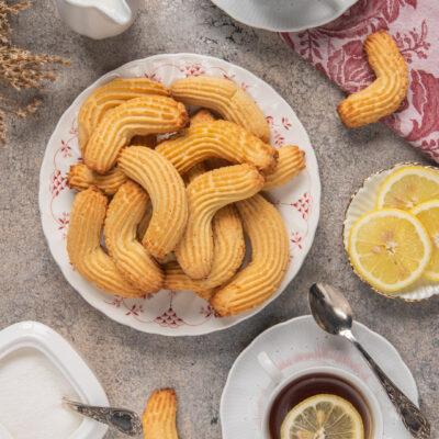 Krumiri dorati a forma di mezzaluna con superficie rigata, serviti accanto a una tazza di tè al limone
