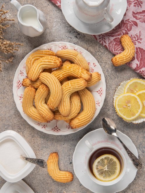 Krumiri dorati a forma di mezzaluna con superficie rigata, serviti accanto a una tazza di tè al limone
