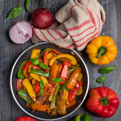 Peperoni in padella saltati con cipolla rossa e foglie di basilico fresco