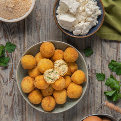 Polpette di ricotta fritte dorate, una spezzata a metà rivela il ripieno con erbe aromatiche