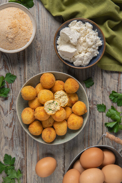 Polpette di ricotta fritte dorate, una spezzata a metà rivela il ripieno con erbe aromatiche