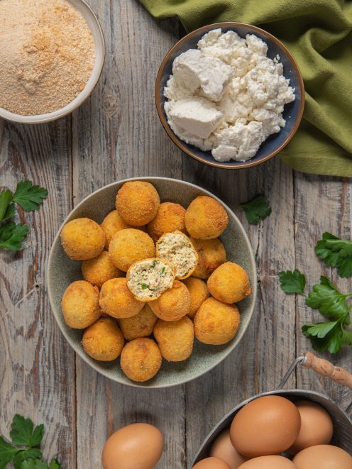 Polpette di ricotta fritte dorate, una spezzata a metà rivela il ripieno con erbe aromatiche