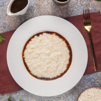 Risotto alla Bergese cremoso al centro del piatto con bordo di riduzione al vino rosso