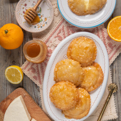 Seadas fritte glassate con miele, ripiene di formaggio, servite con arance e limoni