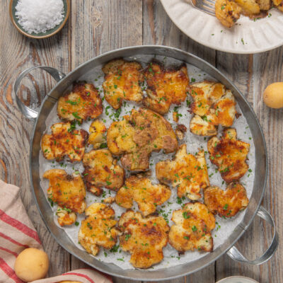 Smashed potatoes dorate e croccanti in teglia, guarnite con erba cipollina tritata