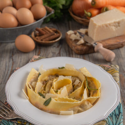 Tagliatelle ripiene arrotolate nel piatto con scaglie di grana e foglie di salvia