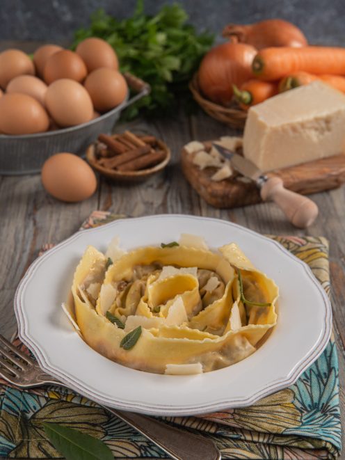 Tagliatelle ripiene arrotolate nel piatto con scaglie di grana e foglie di salvia