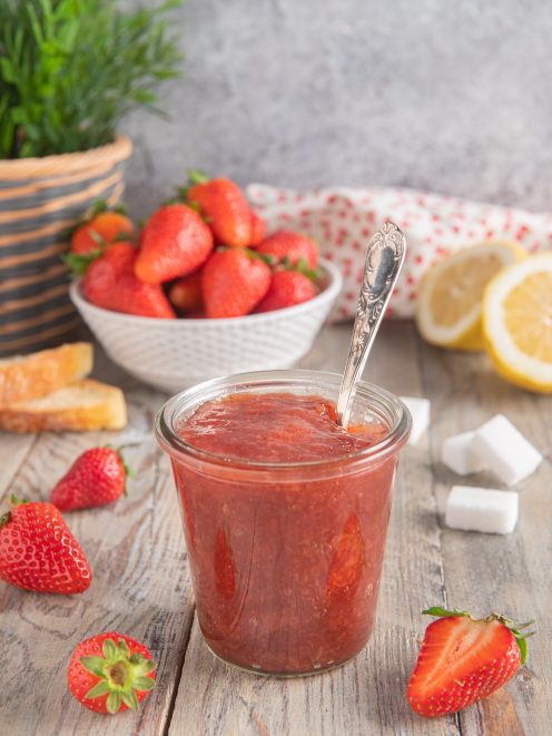 Confettura di fragole in barattolo di vetro con cucchiaino, fragole fresche e limone sullo sfondo