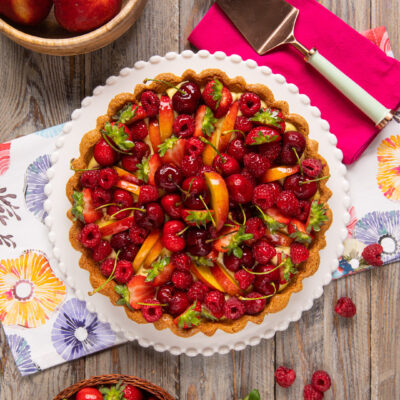 Crostata alla frutta senza glutine guarnita con lamponi, ciliegie, fragole e fette di pesca su crema pasticcera