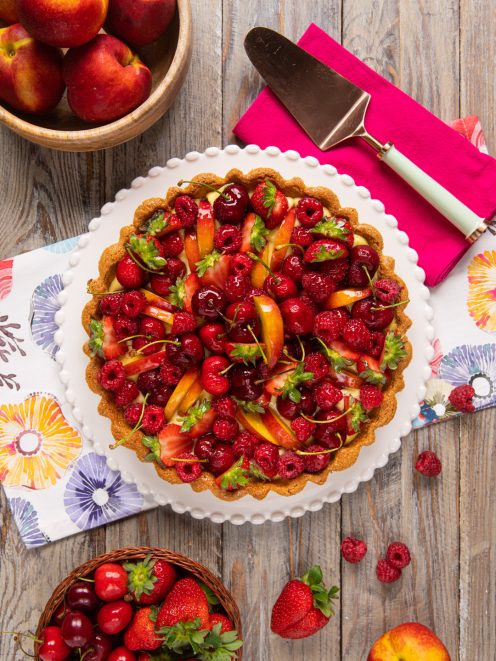 Crostata alla frutta senza glutine guarnita con lamponi, ciliegie, fragole e fette di pesca su crema pasticcera