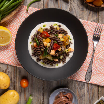 Insalata di pasta tiepida con ortaggi, salmone e burrata su crema vellutata nel piatto