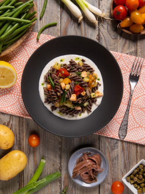 Insalata di pasta tiepida con ortaggi, salmone e burrata su crema vellutata nel piatto