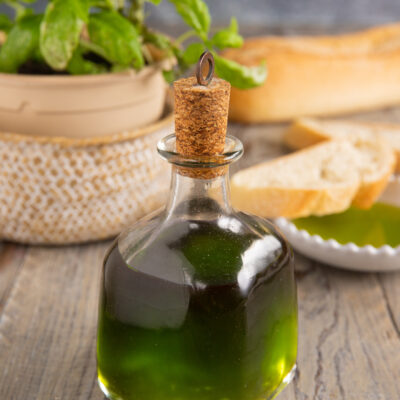 Olio al basilico in bottiglia con tappo di sughero, accanto a fette di pane