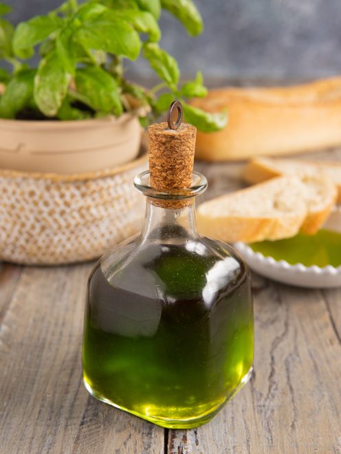 Olio al basilico in bottiglia con tappo di sughero, accanto a fette di pane