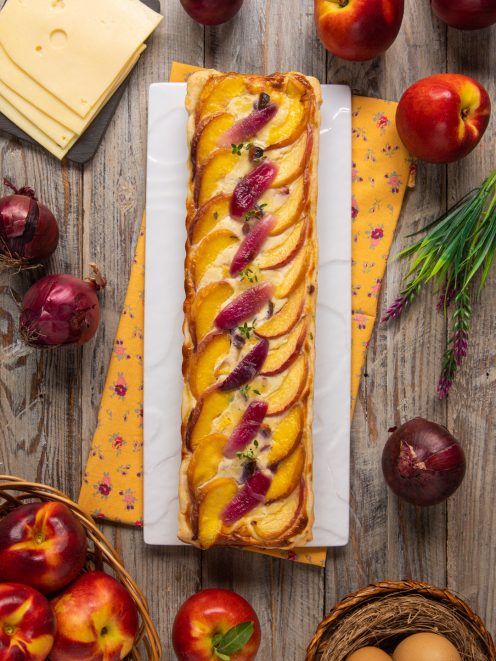 Quiche rettangolare con fette di pesca disposte a ventaglio e listarelle di cipolla rossa caramellata