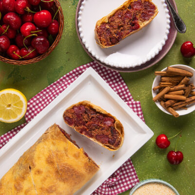 Strudel di ciliegie tagliato a fette con ripieno succoso, servito tra ciliegie fresche e cannella