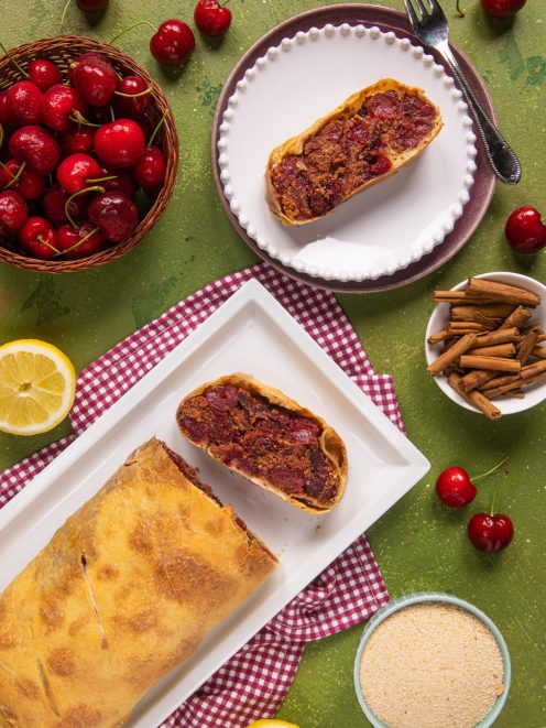 Strudel di ciliegie tagliato a fette con ripieno succoso, servito tra ciliegie fresche e cannella