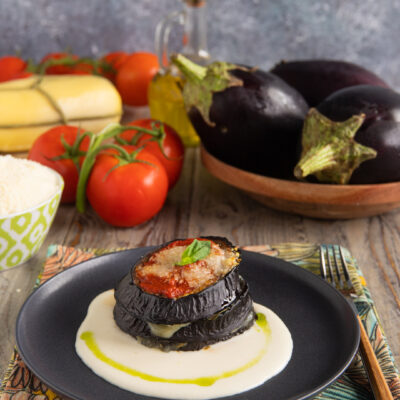 Torretta di melanzane alla parmigiana su crema bianca con filo di olio e basilico fresco