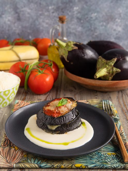 Torretta di melanzane alla parmigiana su crema bianca con filo di olio e basilico fresco