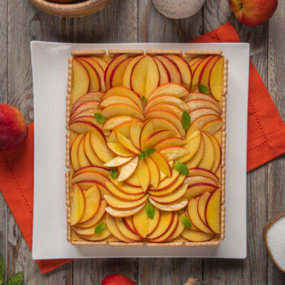 Torta biscotto con crema alle pesche disposte a raggiera e decorata con foglioline di menta