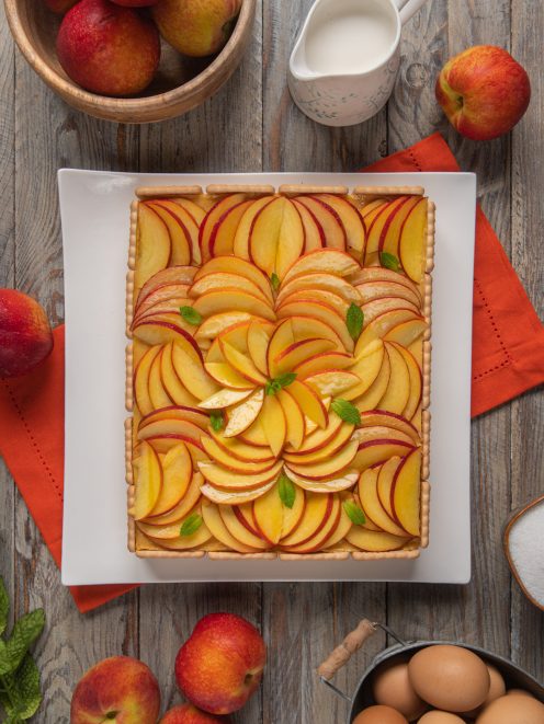 Torta biscotto con crema alle pesche disposte a raggiera e decorata con foglioline di menta
