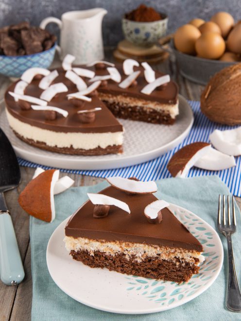 Torta cocco e cioccolato con strati di pan di spagna, crema al cocco e glassa, guarnita con scaglie di cocco fresco