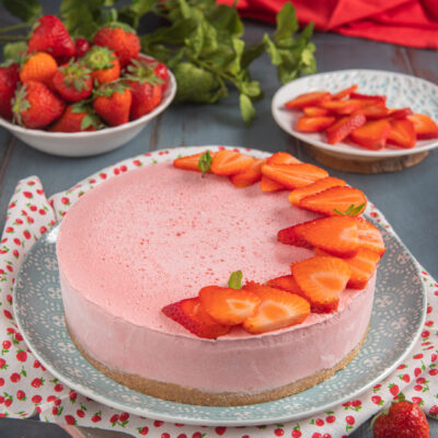 Torta fredda allo yogurt e fragole con base di biscotti, mousse rosa e fette di fragola fresche