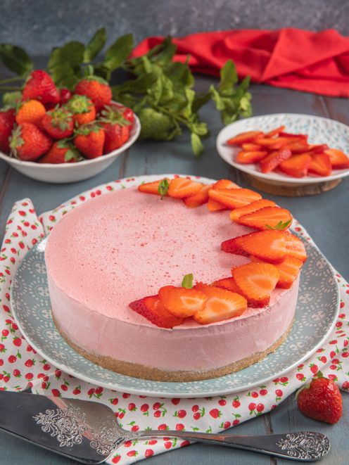Torta fredda allo yogurt e fragole con base di biscotti, mousse rosa e fette di fragola fresche