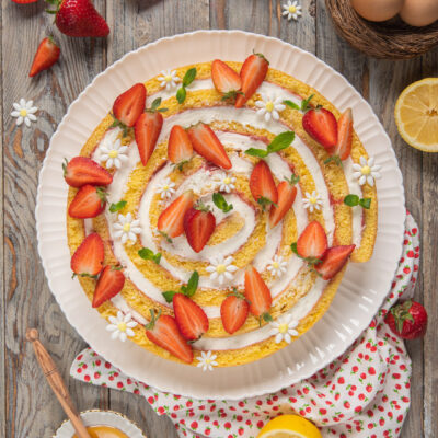 Torta spirale a fette con crema e fragole fresche, vista dall'alto tra fragole e limoni