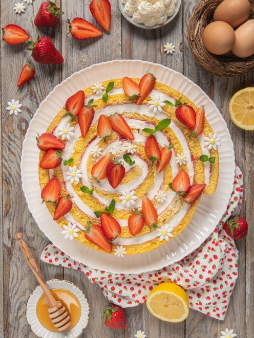 Torta spirale a fette con crema e fragole fresche, vista dall'alto tra fragole e limoni