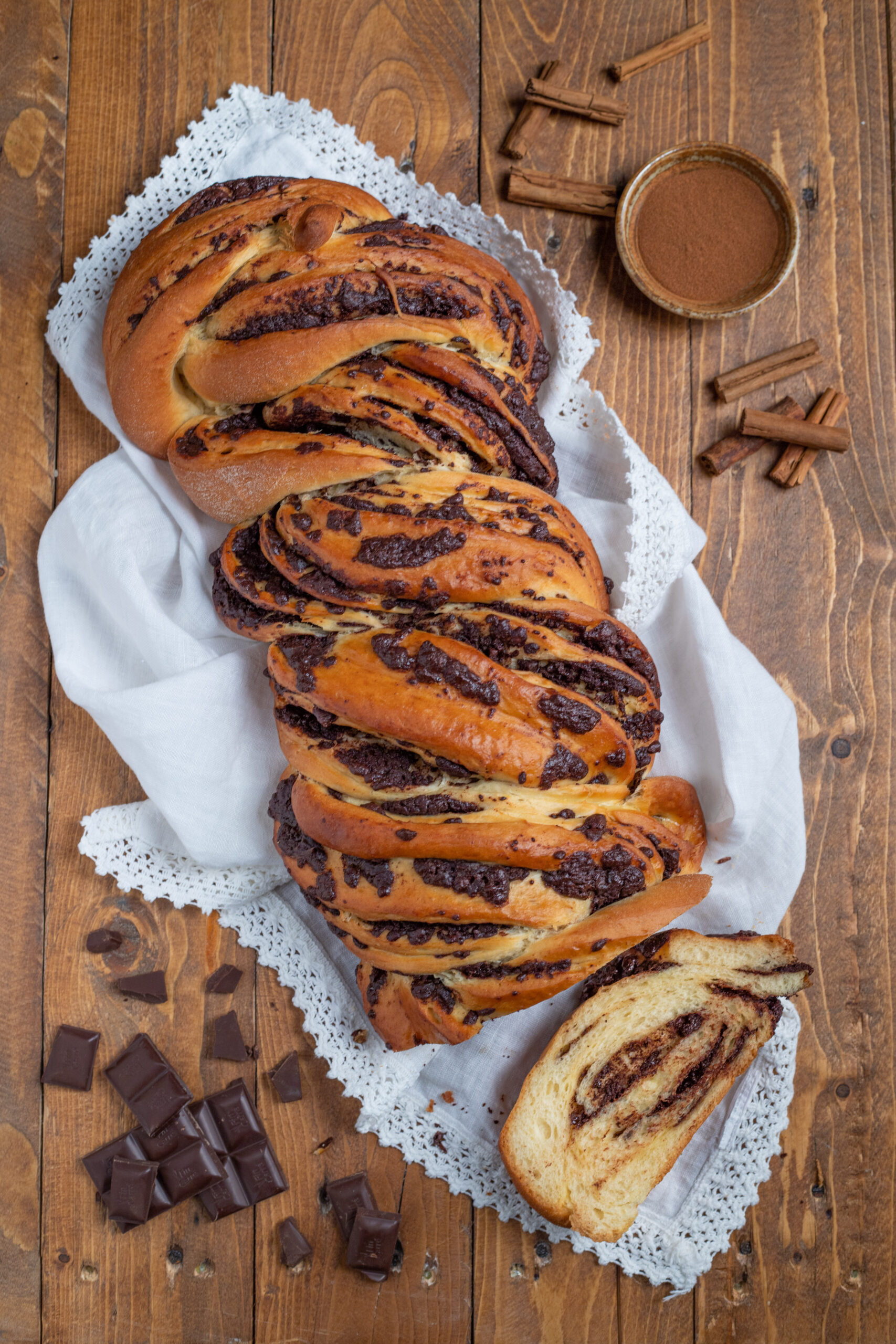 Babka al cioccolato intrecciata e dorata, con una fetta tagliata che mostra la spirale interna